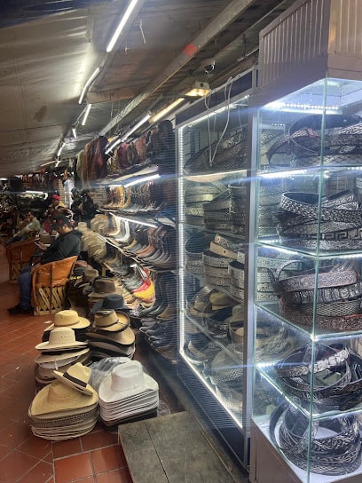 Pasillo del local: vitrinas iluminadas llenas de cinturones enrollados y pilas de sombreros de palma y fieltro en el suelo